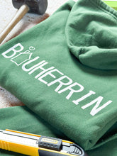 Laden Sie das Bild in den Galerie-Viewer, Dunkelgrüner Pullover Detailansicht hinten. Hier steht die Aufschrift Bauherrin und das A stellt ein Haus dar 
