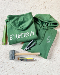 Dunkelgrüner Pullover mit der Aufschrift Bauherrin. Der Pullover hat eine Kapuze und eine Bauchtasche. Der Pullover ist für Männer und Frauen erhältlich.